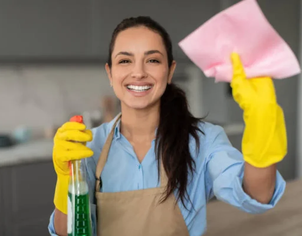 House cleaner in yellow gloves holding a spray bottle and cleaning cloth in a kitchen during a vacation rental turnover in Chandler, AZ.